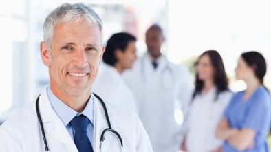 At doctor smiling with his medical marketing team behind him in the background.