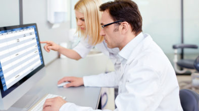 Smiling doctor sits in front of his laptop, checking his social media page for clinical trials recruitment.