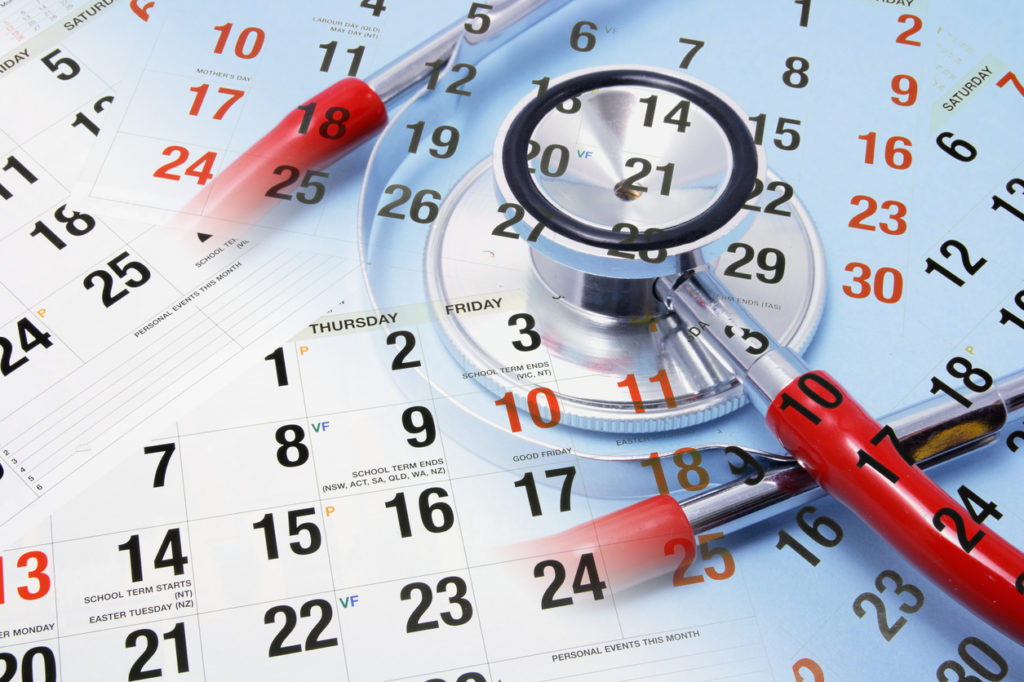 Paper calendars stacked on top of each other to symbolize hectic booking processes before online appointment booking, with a stethoscope and a pen.