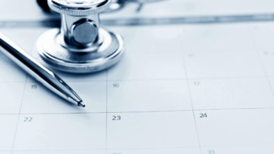 A stethoscope and a pen resting on a conventional paper calendar, to show how appointments were scheduled before online appointment booking.